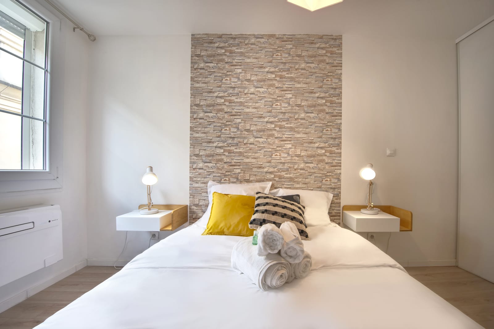 Tête de lit avec papier peint effet pierre et liseuses de chevet, chambre de l'appartement La Balade Nîmoise